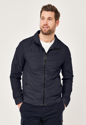 Navy blue zip-up jacket with a stand collar, textured fabric, and front pockets. The design features a plain finish with stitched accents.
