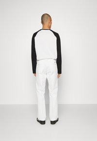 White pants paired with a black and white long-sleeve shirt, viewed from the back. Smooth fabric, straight fit, minimalistic design. Black footwear.