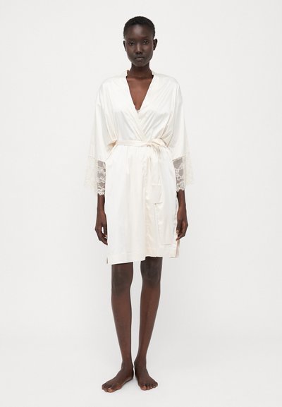 Robe in satin avorio con ampie maniche in pizzo, legato in vita. Presenta un profondo scollo a V e tasche, texture liscia e design fino al ginocchio.