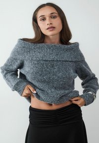 Grijze off-the-shoulder trui met een geribbeld halslijn en zachte textuur, gecombineerd met een zwarte rok met een gerimpeld ontwerp.