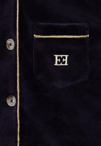 Camicia in velluto blu navy con rifiniture dorate lungo la pattina dei bottoni e la tasca. Presenta un piccolo logo ricamato e dettagli dei bottoni grigi.