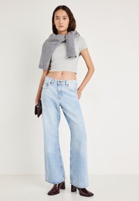 Φαρδιά τζιν παντελόνια σε ανοιχτό μπλε με ψηλή μέση, συνδυασμένα με εφαρμοστό γκρι μπλουζάκι και γκρι πλεκτό κασκόλ που είναι περασμένο στους ώμους.