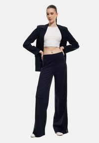 Marina vida byxorna i breda ben är gjorda av mjukt tyg, har hög midja och sidostrimmor. Kombineras med en åtsittande vit crop top och en strukturerad kavaj.