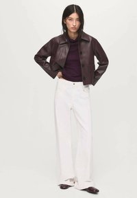 Chaqueta corta de piel burdeos con cuello y botones negros, combinada con pantalones blancos de pierna ancha y zapatos oscuros. Texturas suaves, ajuste moderno.