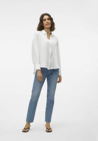White long-sleeve button-up shirt with a textured finish, paired with light blue straight-leg jeans and black flat sandals.