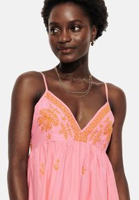 Robe rose avec broderies orange. Dotée d'un décolleté en V, de fines bretelles et d'une jupe froncée, mettant en valeur des motifs floraux et des textures.