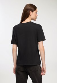 Czarna koszulka z krótkim rękawem wykonana z bawełny, posiadająca luźny krój, okrągły dekolt oraz gładką fakturę z minimalnymi detalami szwów.