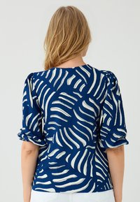 Blusa strutturata blu navy con motivi astratti a onde bianche, maniche a sbuffo e scollatura rotonda. Adatta per abbigliamento casual.