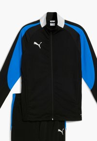 Crna i plava atletska trenerka, koja se sastoji od jakne s patentnim zatvaračem i bijelim ovratnikom te Puma logotipom, u kombinaciji s odgovarajućim crnim hlačama.