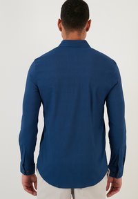 Ciemnoniebieska koszula z długim rękawem o teksturowanej tkaninie, z wyrazistym kołnierzykiem, zapinanymi mankietami i zaokrąglonym dołem w talii.