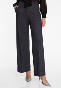 Wijde broek in donkergrijze krijtstreep stof, met een hoge taille, zijzakken en opgerolde manchetten. Gecombineerd met zilveren stiletto hakken.