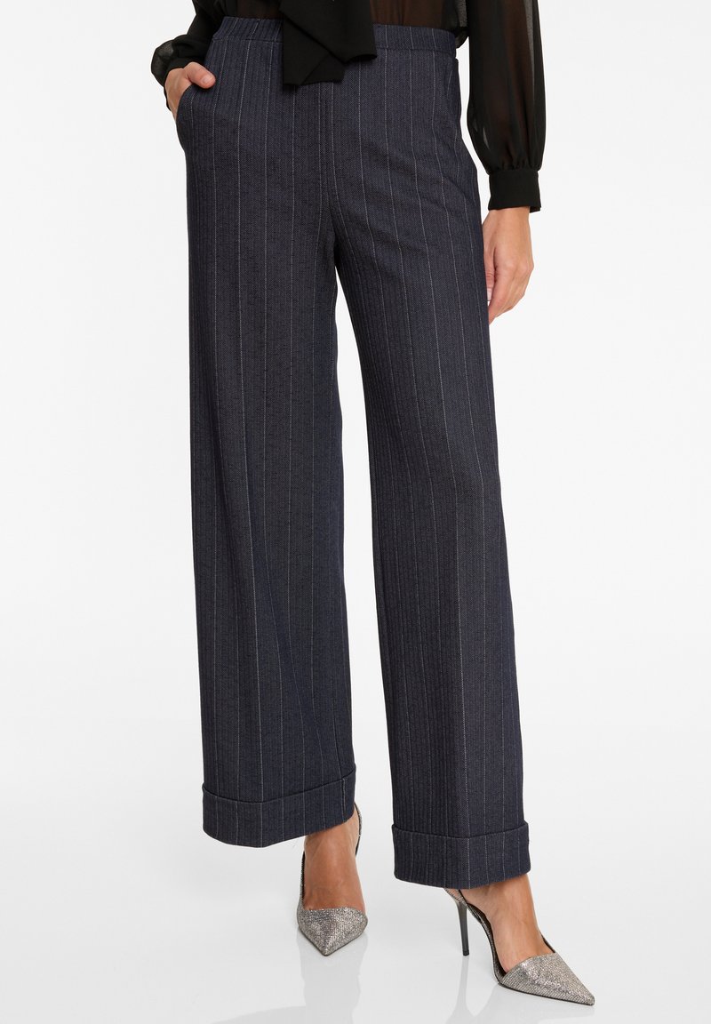 Wijde broek in donkergrijze krijtstreep stof, met een hoge taille, zijzakken en opgerolde manchetten. Gecombineerd met zilveren stiletto hakken.