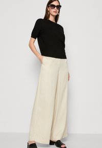 Top scurt negru cu mâneci scurte combinat cu pantaloni largi crema. Ţinuta are o textură fină și un design simplu, curat. Sandale negre cu toc.