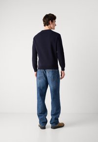 Navy blue knitted sweater with long sleeves, fitted cuffs, and a simple round neckline, paired with loose light blue jeans and brown shoes.
