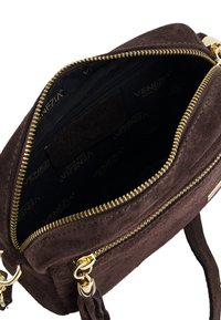 Brun suedette håndtaske med gyldne lynlåse, der har en tekstureret indvendig med et logo mønster og to lynlåslommer til organisering.