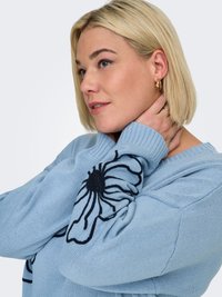 Pull tricoté bleu clair avec broderie florale noire sur les manches. Il présente un col côtelé et un tissu texturé.