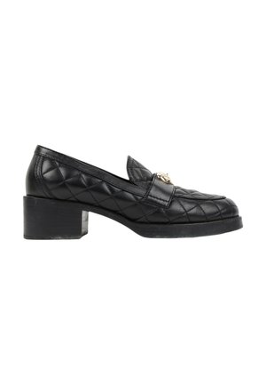Mocassin en cuir noir matelassé avec talon bloc et emblème décoratif doré à l'avant, présenté de profil sur fond blanc.