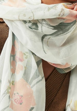 Foulard léger et transparent avec un imprimé floral rose doux et vert, enroulé autour d'une personne portant un vêtement marron en tricot.