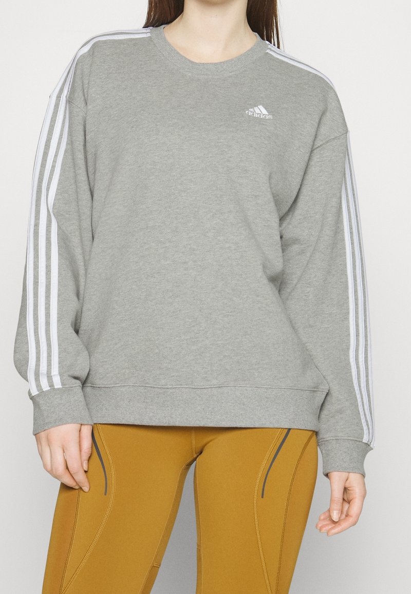 Kvinna som bär en grå Adidas-tröja med vita ränder på ärmarna och senapsgula träningsleggings med svarta sömdetaljer.