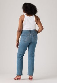 Høyt midjet blå denim jeans med rett passform, med skinnlapp bak og doble baklommer; brukt med en hvit tanktopp.
