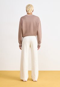 Túlméretezett barna pulóver bordás nyakkivágással és krém színű, széles lábú sportnadrággal. Simító anyag, amely két színű díszítéssel rendelkezik a mandzsettán.