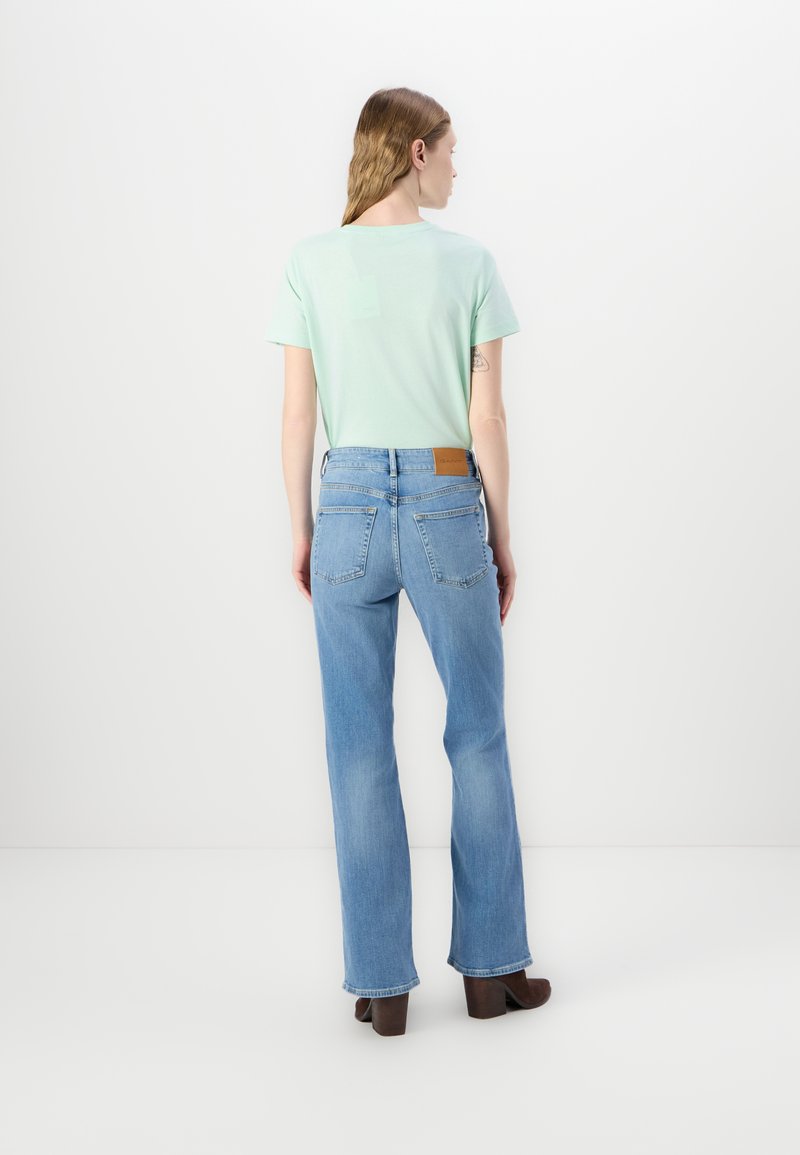 Miętowozielona bluzka z krótkim rękawem w połączeniu z jasnoniebieskimi spodniami dzwonami. Spodnie mają brązową skórzaną łatę przy pasku.