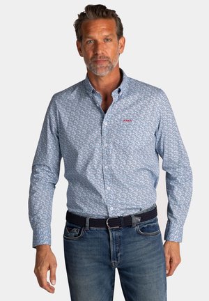 Lichtblauwe overhemdd met kleine bloemenpatronen, lange mouwen en een rood geborduurd logo. Gecombineerd met donkerblauwe spijkerbroeken en een riem.