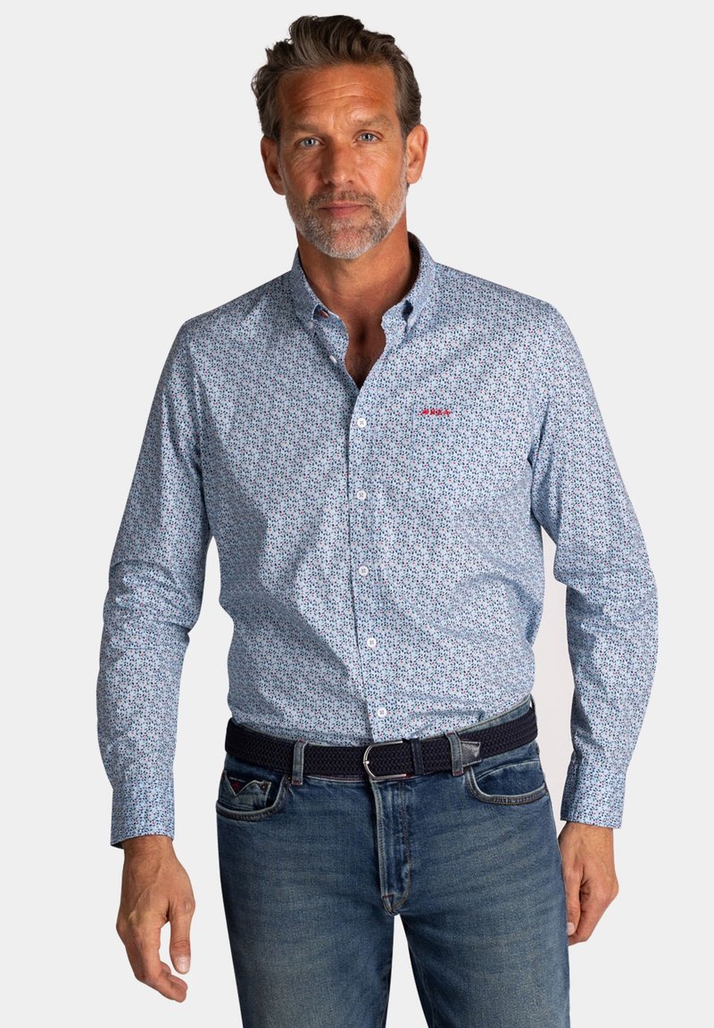 Lichtblauwe overhemdd met kleine bloemenpatronen, lange mouwen en een rood geborduurd logo. Gecombineerd met donkerblauwe spijkerbroeken en een riem.