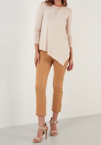 Top rosa chiaro a maniche lunghe con orlo asimmetrico, abbinato a pantaloni fitted color sabbia e sandali con tacco beige. Texture semplici e lisce.