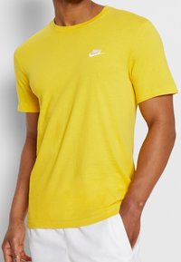 Yellow cotton t-shirt with a round neckline, short sleeves, and a small white Nike logo embroidered on the left chest. Smooth texture.