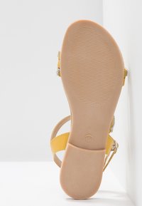 Sandale avec semelle en caoutchouc beige et lanières en cuir jaune, marquage de taille visible "37" sur la semelle, positionnée debout sur un fond blanc.