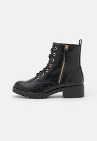 Bottine noire à lacets avec une texture crocodile, fermeture éclair sur le côté, accents en métal doré et talon épais. Semelle en caoutchouc durable.