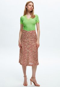 Top corto a righe verdi abbinato a una gonna al ginocchio con stampa leopardata rossa e rosa. La modella indossa sandali con tacco beige.