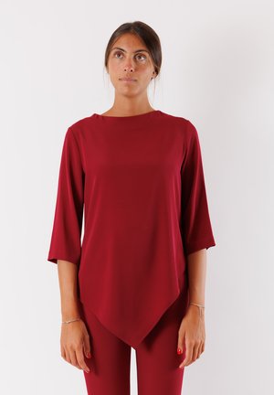 Tunic bordeaux con scollatura rotonda e maniche a tre quarti, caratterizzata da un'unica orlo asimmetrico e tessuto liscio e fluido.