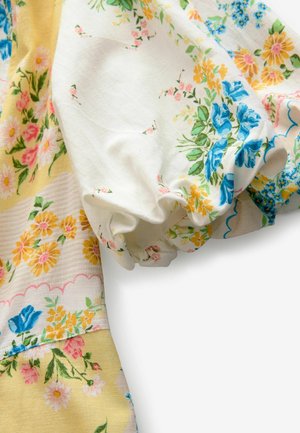 Tissu à motifs floraux comportant des tons blancs, jaunes et bleus. Volants élastiques le long des manches et surface douce au toucher.