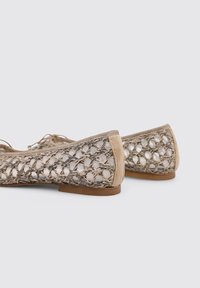 Bailarinas tejídas en color beige con un diseño de malla abierta texturizada y acentos de cuero liso en tono marrón, que presentan un perfil bajo y punta redondeada.