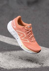 La sneaker présente un dessus en maille légère de couleur pêche, une semelle en caoutchouc blanche, des détails en relief et un logo proéminent sur le côté.