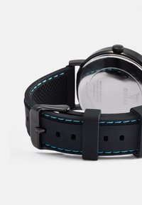 Cinturino in gomma nera con cuciture blu a contrasto, fibbia in metallo, superficie inferiore testurizzata e retro in acciaio inossidabile riflettente.