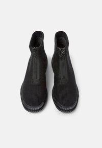 Svarta zip-up ankelskängor tillverkade av texturerat tyg, med en gummisula och rund tå. Dragkedjan går centralt längs framsidan.