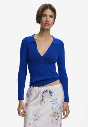 Blue ribbed cardigan with long sleeves, v-neck, and buttons down the front, paired with a floral-patterned skirt featuring pastel colors.
