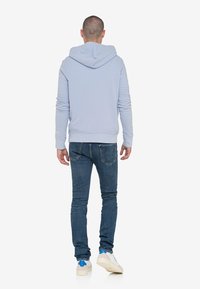 Sudadera azul claro con capucha y cordones, puños acanalados, combinada con jeans de mezclilla oscura y zapatillas blancas con acentos azules.