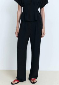 Černý peplum top s krátkým rukávem a širokými kalhotami ve stejném stylu. Nosič má na sobě červené žabky. Texturovaná tkanina.