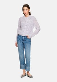 Helllila gestrickte Strickjacke mit einem diamantförmigen Spitzenmuster, rundem Ausschnitt und Knopfverschluss, kombiniert mit blauen, umgeschlagenen Jeans und grauen Ballerinas.