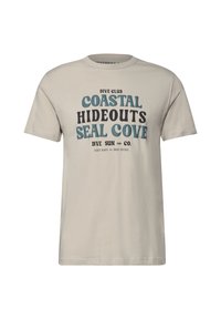 Světle béžové bavlněné tričko s krátkým rukávem. Na přední straně se nachází modrý a černý text s nápisem "DIVE CLUB COASTAL HIDEOUTS SEAL COVE."