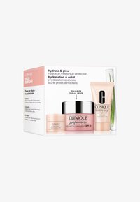 Le set de soins Clinique comprend un pot rose de 50 ml, une crème pour les yeux de 15 ml et un masque de nuit de 30 ml, présenté dans une boîte blanche et rose avec du texte.