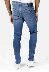 Slim-fit blue denim jeans featuring a mid-rise waist, back pockets, and a black leather logo patch on the waistband.