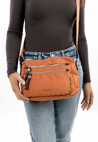 Oranžová crossbody taška vyrobená z měkké tkaniny s několika zipovými přihrádkami. Obsahuje logo a nastavitelný ramenní popruh.