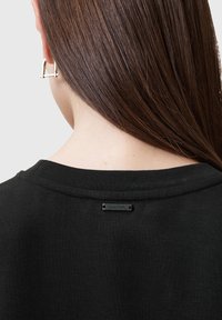 Sudadera negra con un cuello acanalado y una pequeña etiqueta de la marca en la parte posterior. La tela parece suave y cómoda.