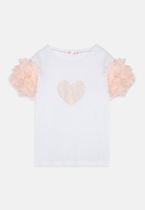 T-shirt blanc avec de courtes manches froncées en pêche et un design en forme de cœur perforé à l'avant. Matière en coton doux, coupe décontractée.