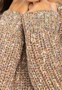 Pull en tricot avec un motif texturé multicolore en beige, rose et vert. Les manches surdimensionnées présentent des coutures variées et offrent une sensation de confort.